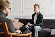A teenage boy in a counseling session discussing with a therapist in an office setting.